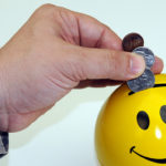 Caucasion hand and arm dressed in military camouflage placing coins in a yellow piggy bank