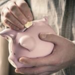 Hands of caucasian man placing a coin in a pink piggy bank